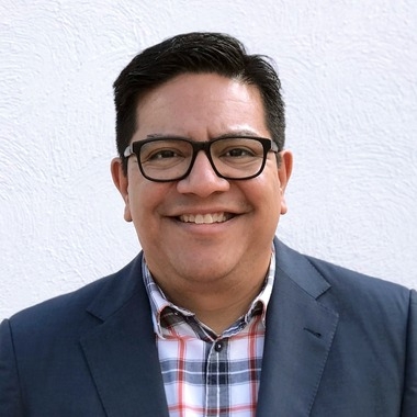 Portrait of a man with brown hair and glasses on a flat gray background.